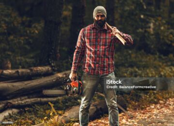 Lumberjack worker standing in the forest with axe and chainsaw
