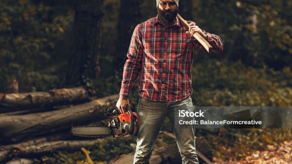 Lumberjack worker standing in the forest with axe and chainsaw